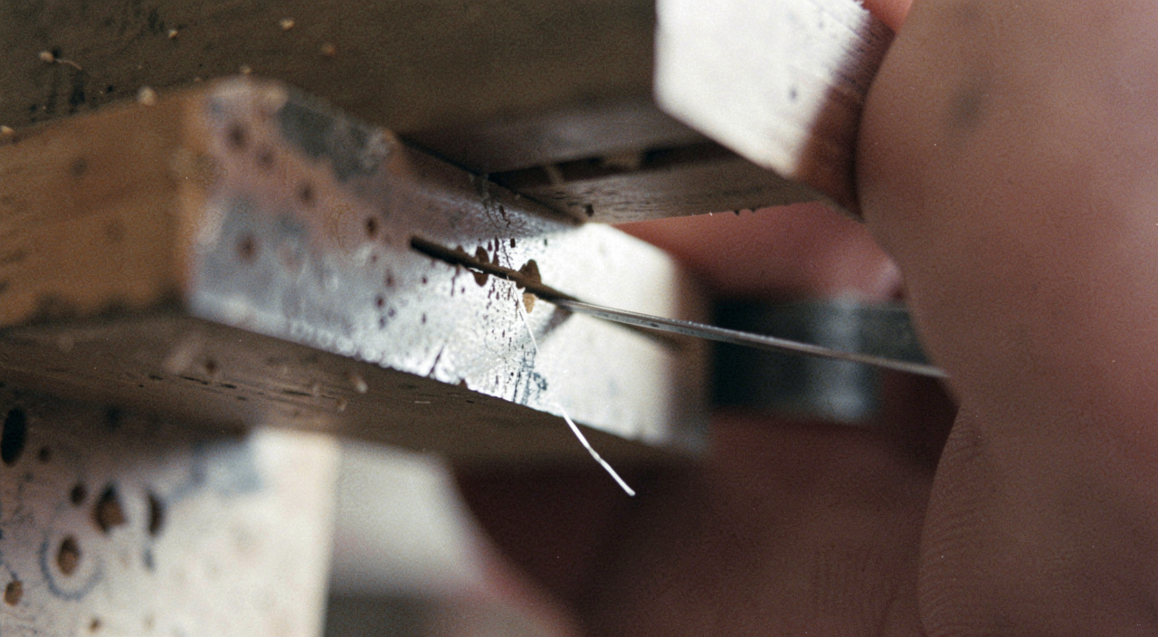 A very close view of the underside of a block plane showing the narrow slot between the sliding mouth plate and the blade edge, a thin shaving emerging, hard task light from one side.