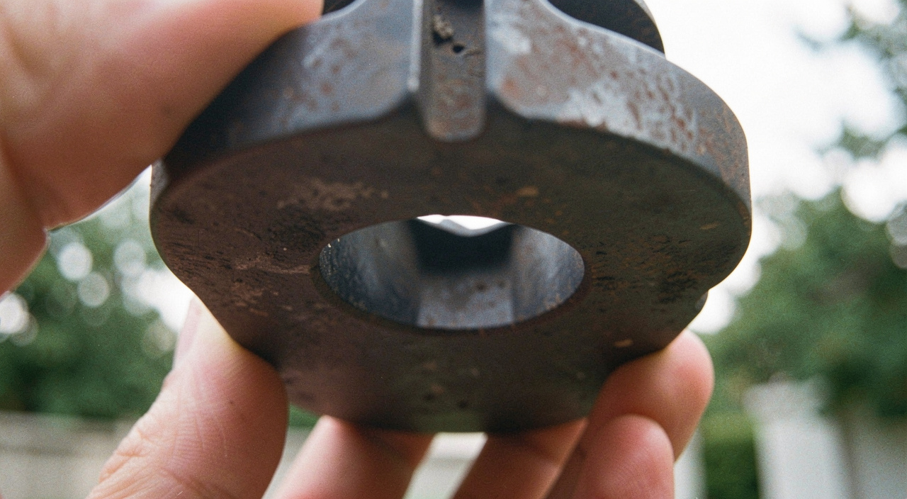 A close view of the underside of a cast iron plane body held up to the light, the narrow bridge of metal in front of the blade opening filling the frame, outdoor daylight.